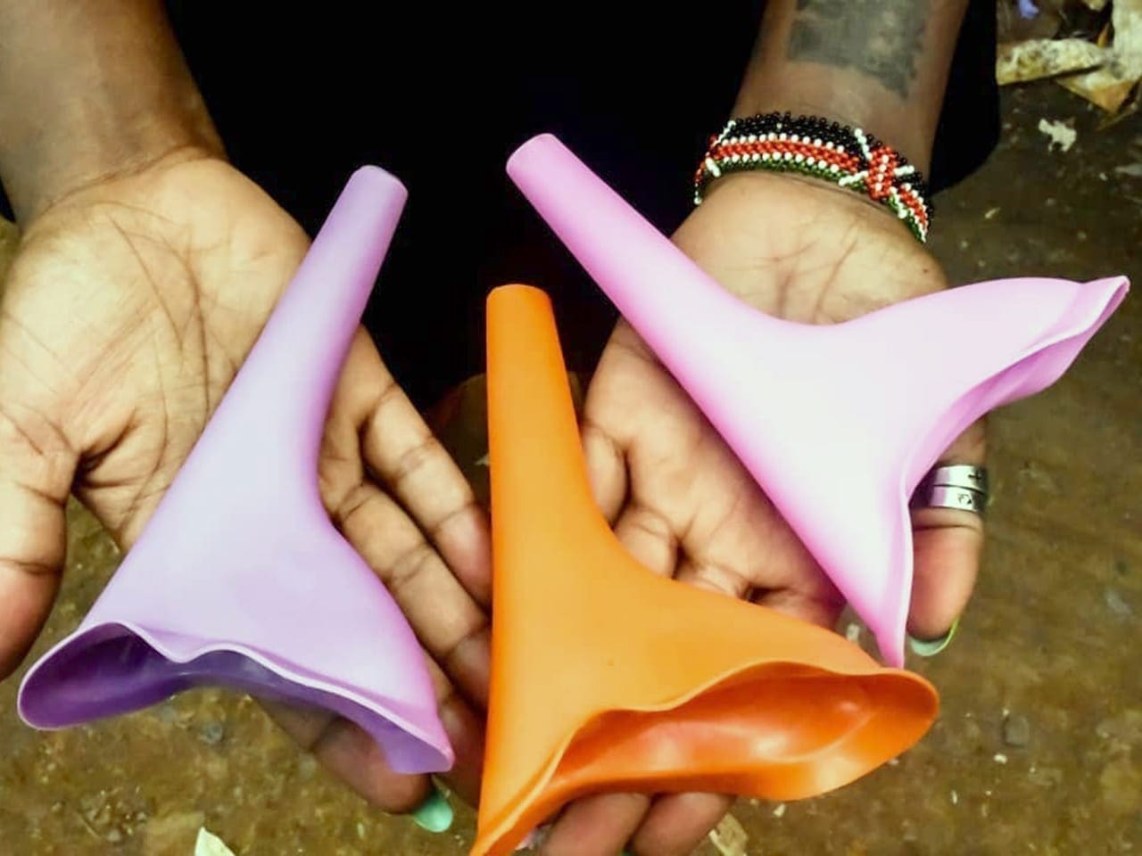 A woman displays three female peeing funnels, two of which are pink while one is orange.